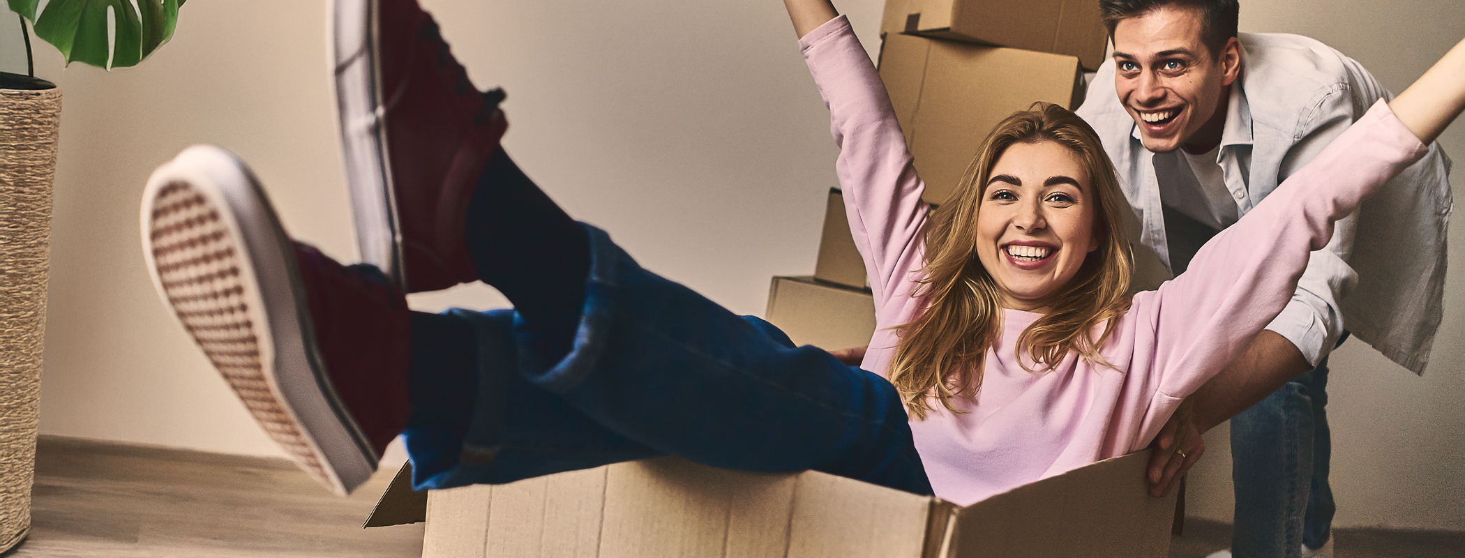 Blij stel viert een stressvrije verhuizing met opgestapelde verhuisdozen op de achtergrond.